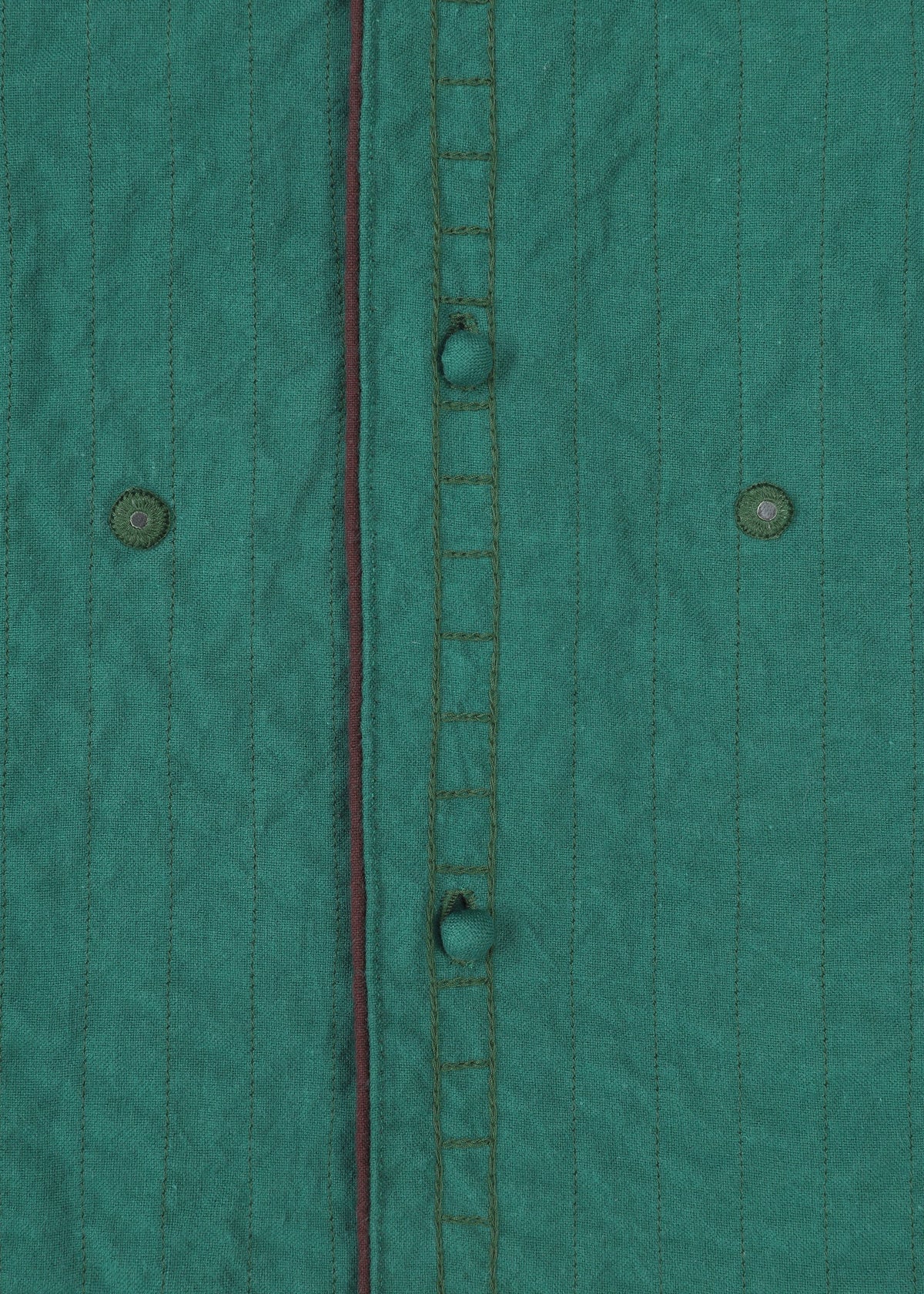 Close-up of HaaT's DUAL LAYER: a handwoven cotton jacket in green with vertical stitched lines, visible buttonholes, two green buttons, and a thin dark red trim along the seam. view 5 of 8