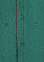 Close-up of HaaT's DUAL LAYER: a handwoven cotton jacket in green with vertical stitched lines, visible buttonholes, two green buttons, and a thin dark red trim along the seam.