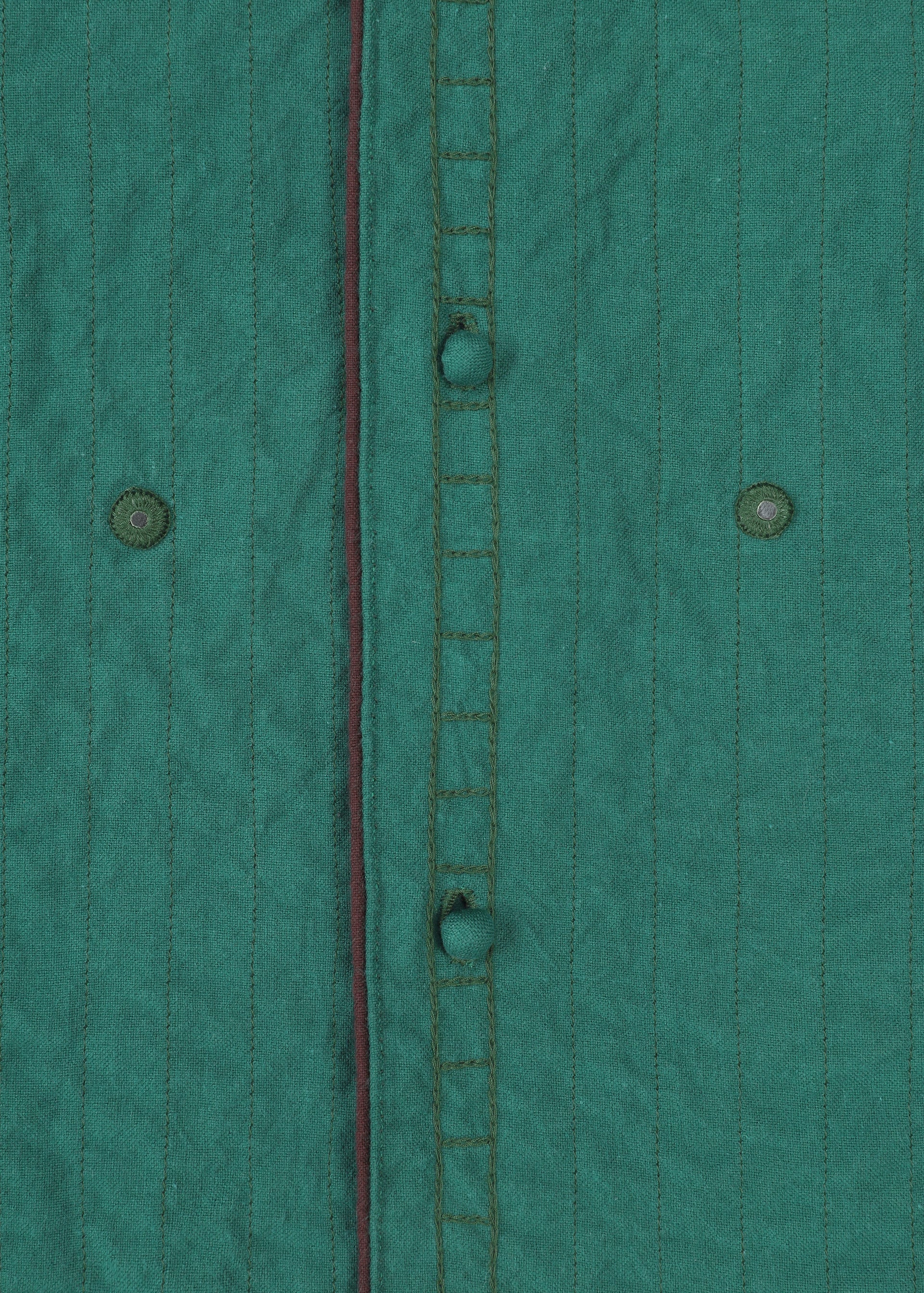 Zoomed view Close-up of HaaT's DUAL LAYER: a handwoven cotton jacket in green with vertical stitched lines, visible buttonholes, two green buttons, and a thin dark red trim along the seam.