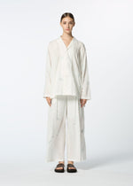 A person faces forward in HaaT’s DAMI LEAVES: a loose white pajama set with Chikan embroidery on the long-sleeve shirt and wide-leg pants. They wear black slide sandals, hair slicked back, and pose against a plain white background.