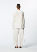 A person stands with their back to the camera, wearing HaaT's DAMI LEAVES loose white long-sleeve shirt with delicate Chikan embroidery and wide-leg pants, paired with dark slip-on sandals, set against a plain light background.