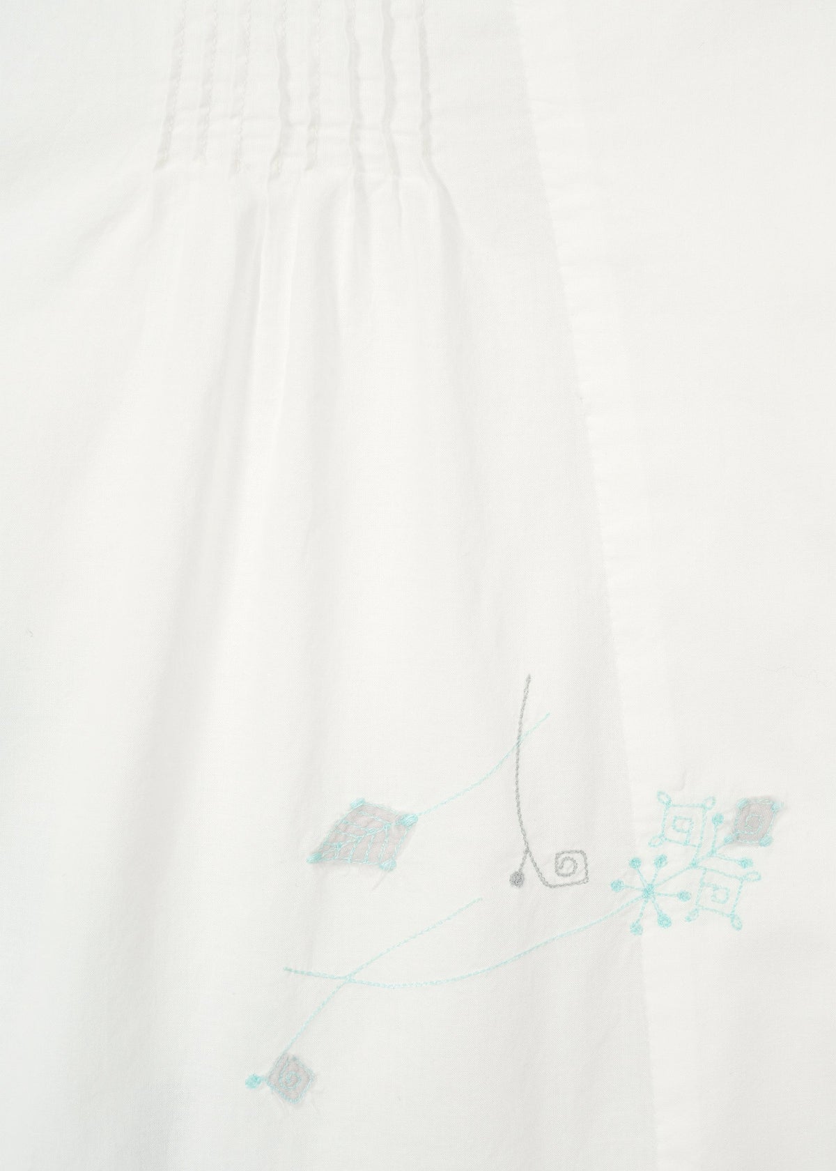 Close-up of white fabric on the DAMI LEAVES long-sleeve shirt by HaaT, featuring subtle top pleats and light blue and gray Chikan embroidery in geometric and swirl patterns near the bottom right. view 6 of 10