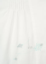 Close-up of white fabric on the DAMI LEAVES long-sleeve shirt by HaaT, featuring subtle top pleats and light blue and gray Chikan embroidery in geometric and swirl patterns near the bottom right.