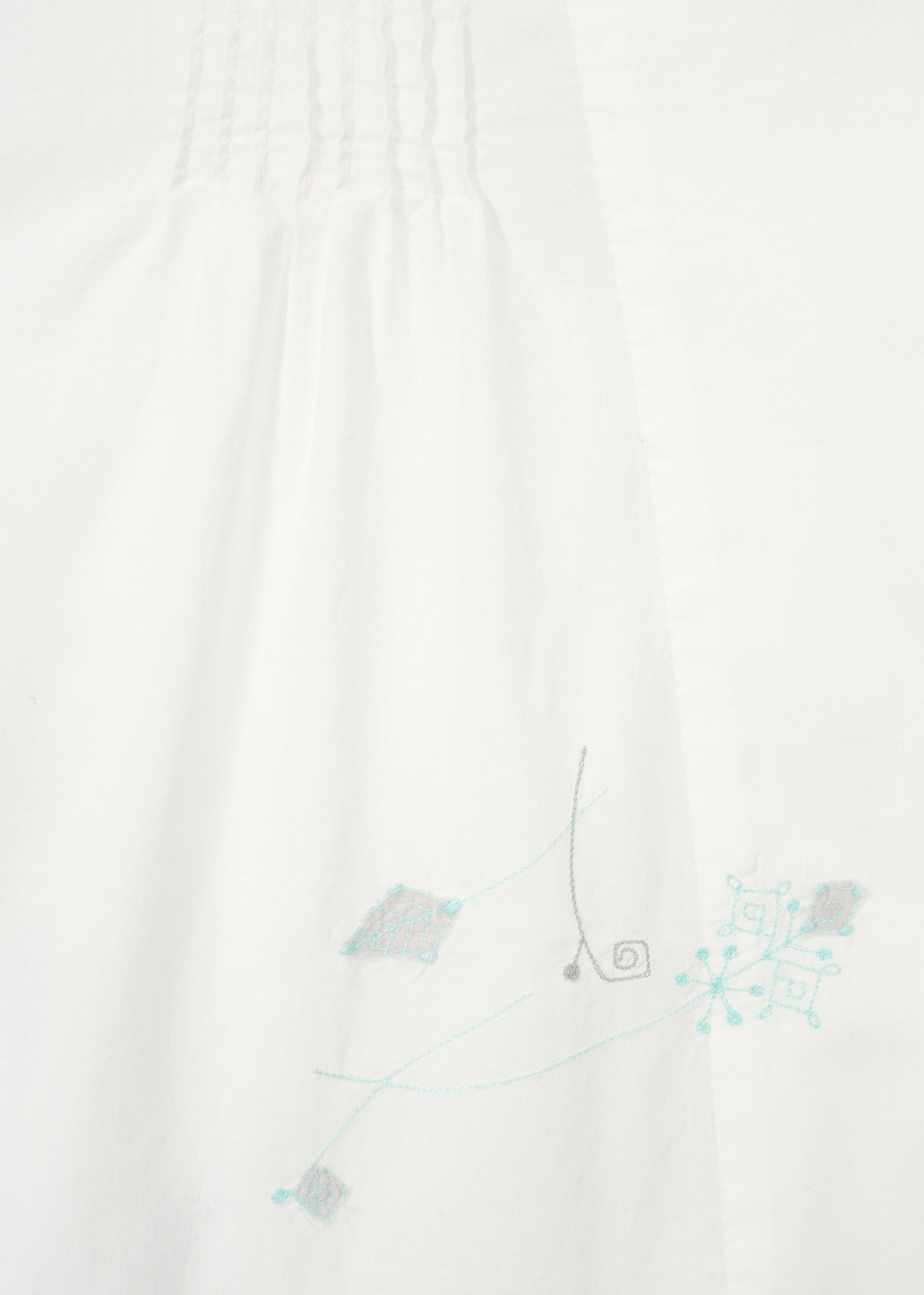 Zoomed view Close-up of white fabric on the DAMI LEAVES long-sleeve shirt by HaaT, featuring subtle top pleats and light blue and gray Chikan embroidery in geometric and swirl patterns near the bottom right.