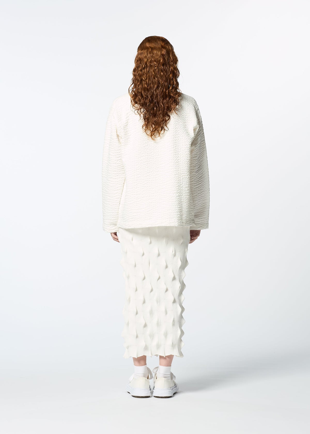 A person with long, curly brown hair faces away, wearing HaaT's 3 MUL MACHINE KABIRA '26SS—a collarless embroidered shirt, white textured skirt, and white sneakers—set against a plain white background. view 8 of 9