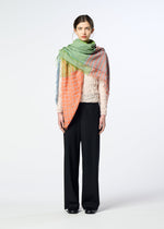 A woman faces forward in a textured light top, black wide-leg pants, black shoes, and the HaaT TRIPLY SQUARE STOLE with hand-finished fringe draped over her shoulders against a plain light background.