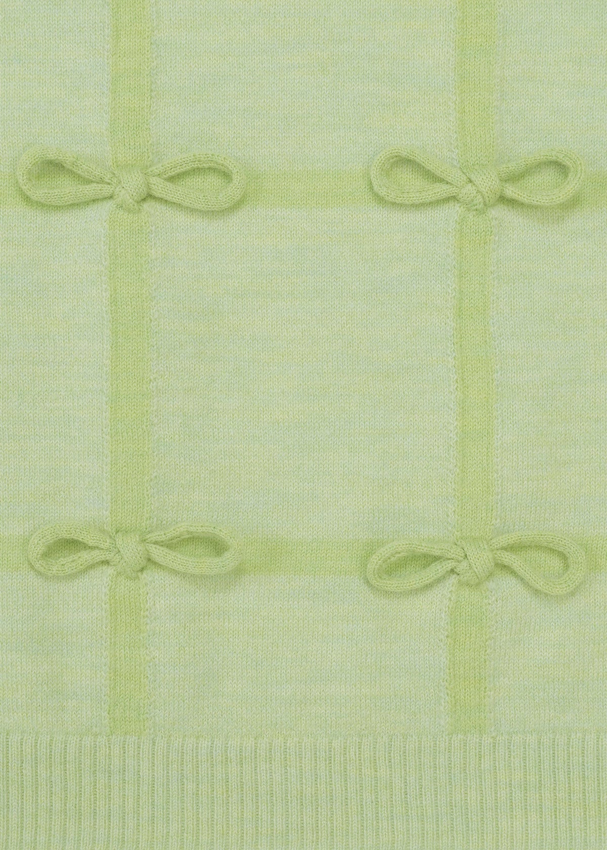Zoomed view RIBBON KNIT by HaaT: A light green knit with a grid pattern and hand-tied bows at each intersection. The soft texture has a slightly ribbed bottom edge, echoing the look of a fulled wool stole.