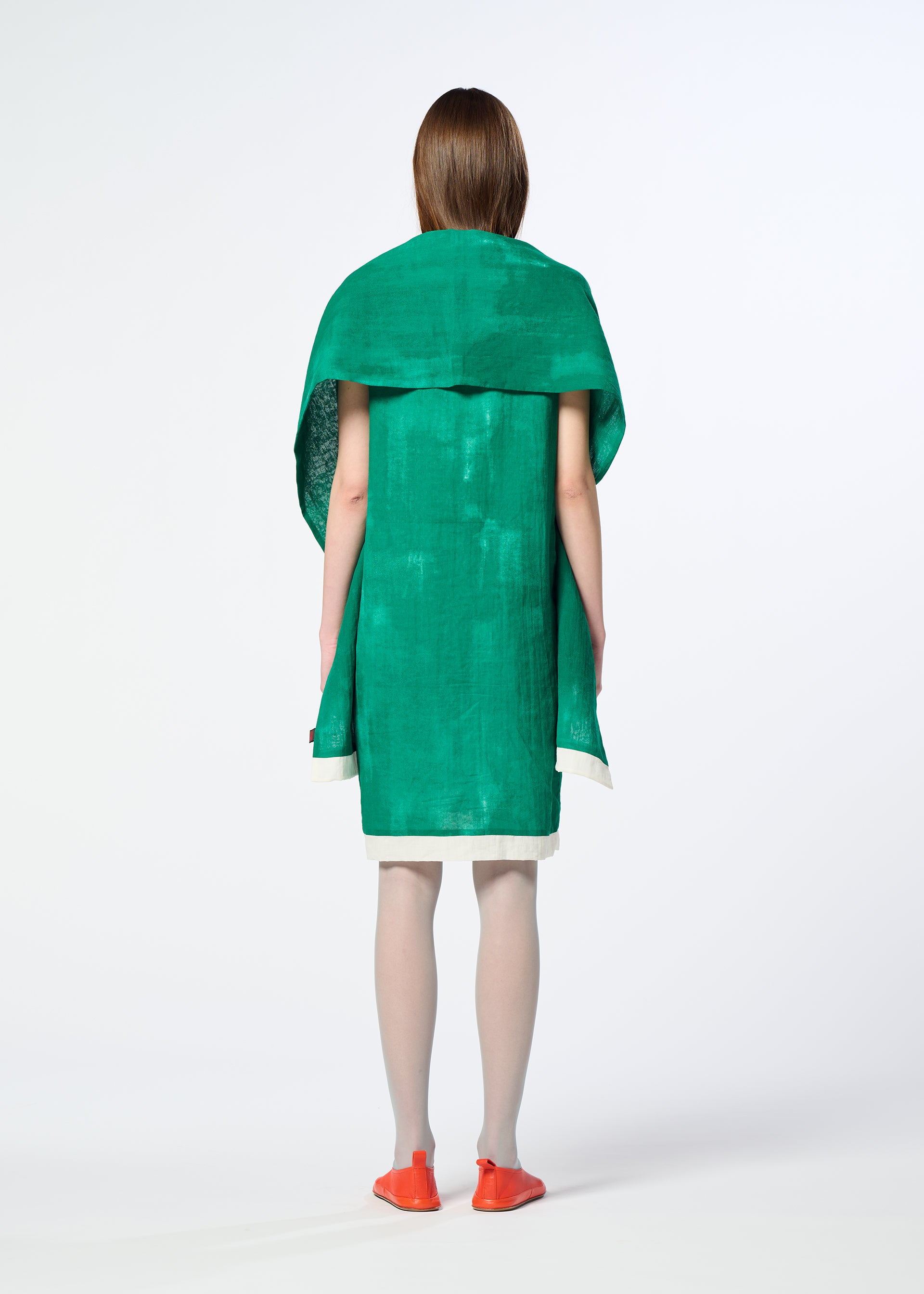 Zoomed view A person stands with their back to the camera, wearing the HaaT WALL WHITE HEM dress—vibrant green with an oversized collar or chiffon stole—paired with white tights and orange flats, set against a plain white background.