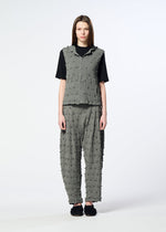 A model stands facing forward against a plain white background, wearing the HaaT KYO CHIJIMI SQUARE EMB set—a textured gray vest featuring embroidered square patterns, paired with matching pants over a black shirt. They have straight brown hair and are wearing black shoes.