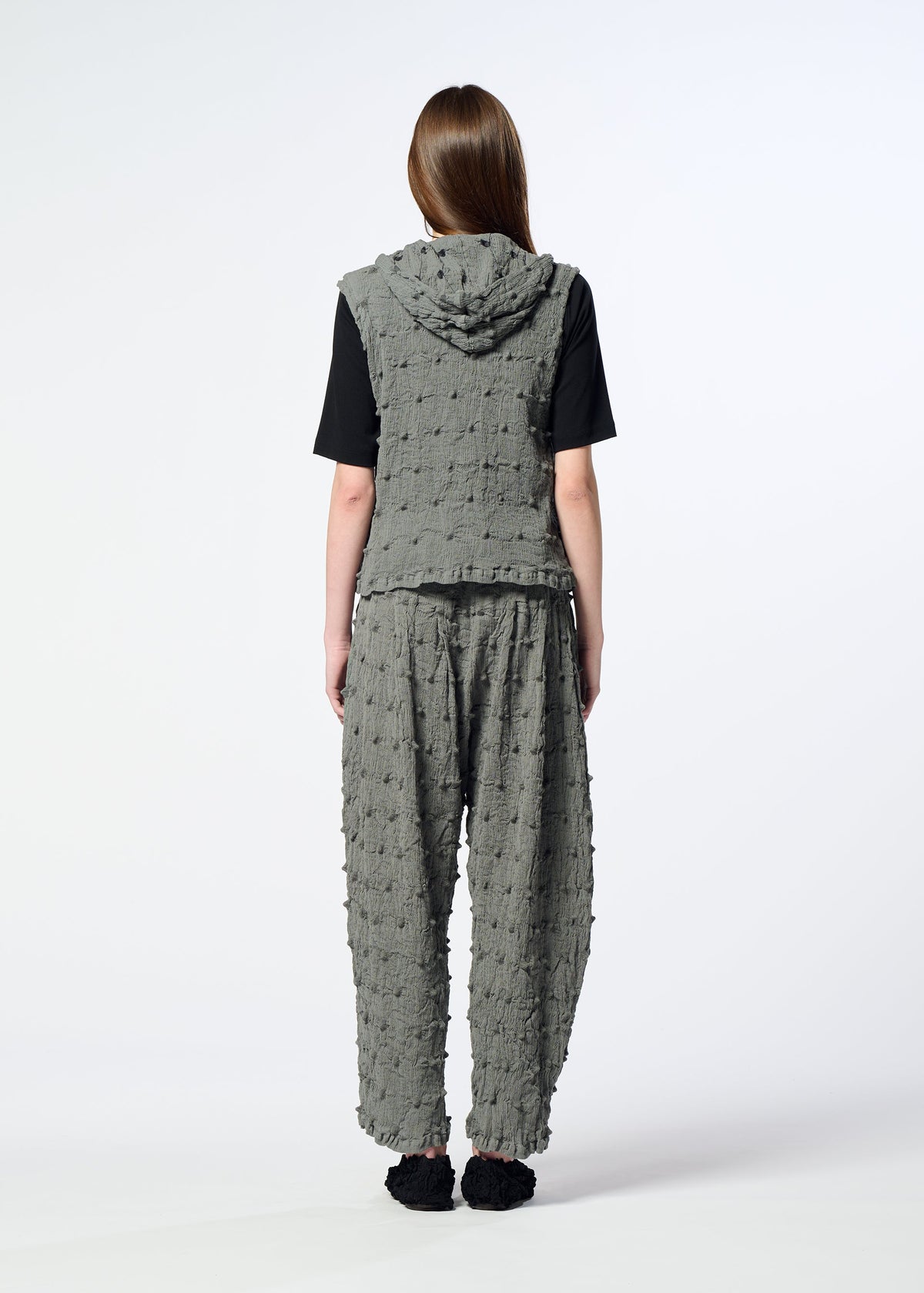 A person stands with their back to the camera, wearing the HaaT KYO CHIJIMI SQUARE EMB textured gray hooded vest and matching loose pants over a black shirt, set against a plain white background. view 9 of 10