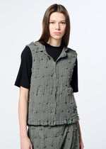A person with straight brown hair wears the HaaT KYO CHIJIMI SQUARE EMB vest—a textured gray sleeveless piece featuring subtle embroidered square patterns—over a black shirt. They stand against a plain light background, looking at the camera with a neutral expression.