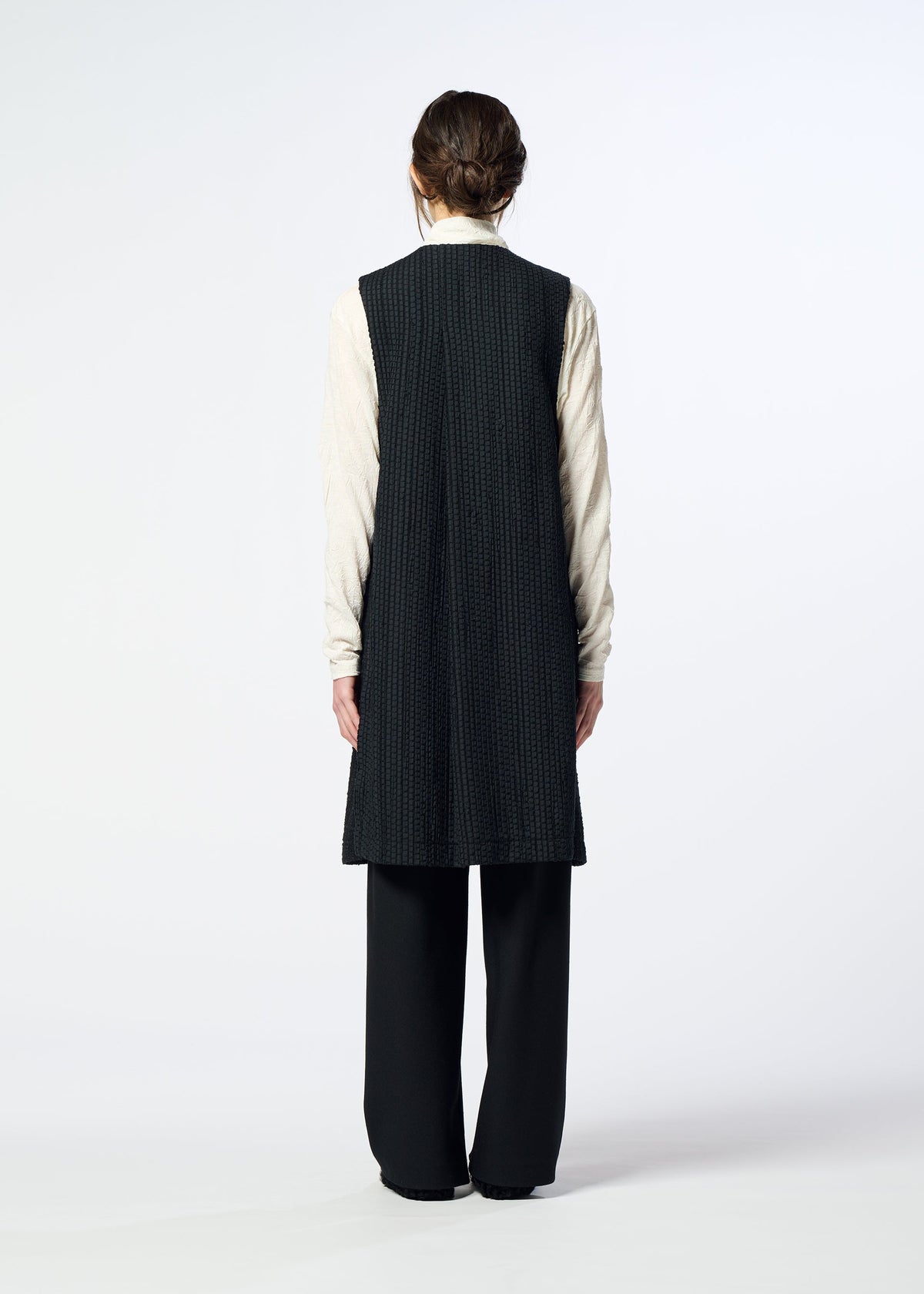 A person faces away, wearing the HaaT SAKIORI long black sleeveless vest over a light long-sleeve shirt and black pants against a plain background. view 10 of 10