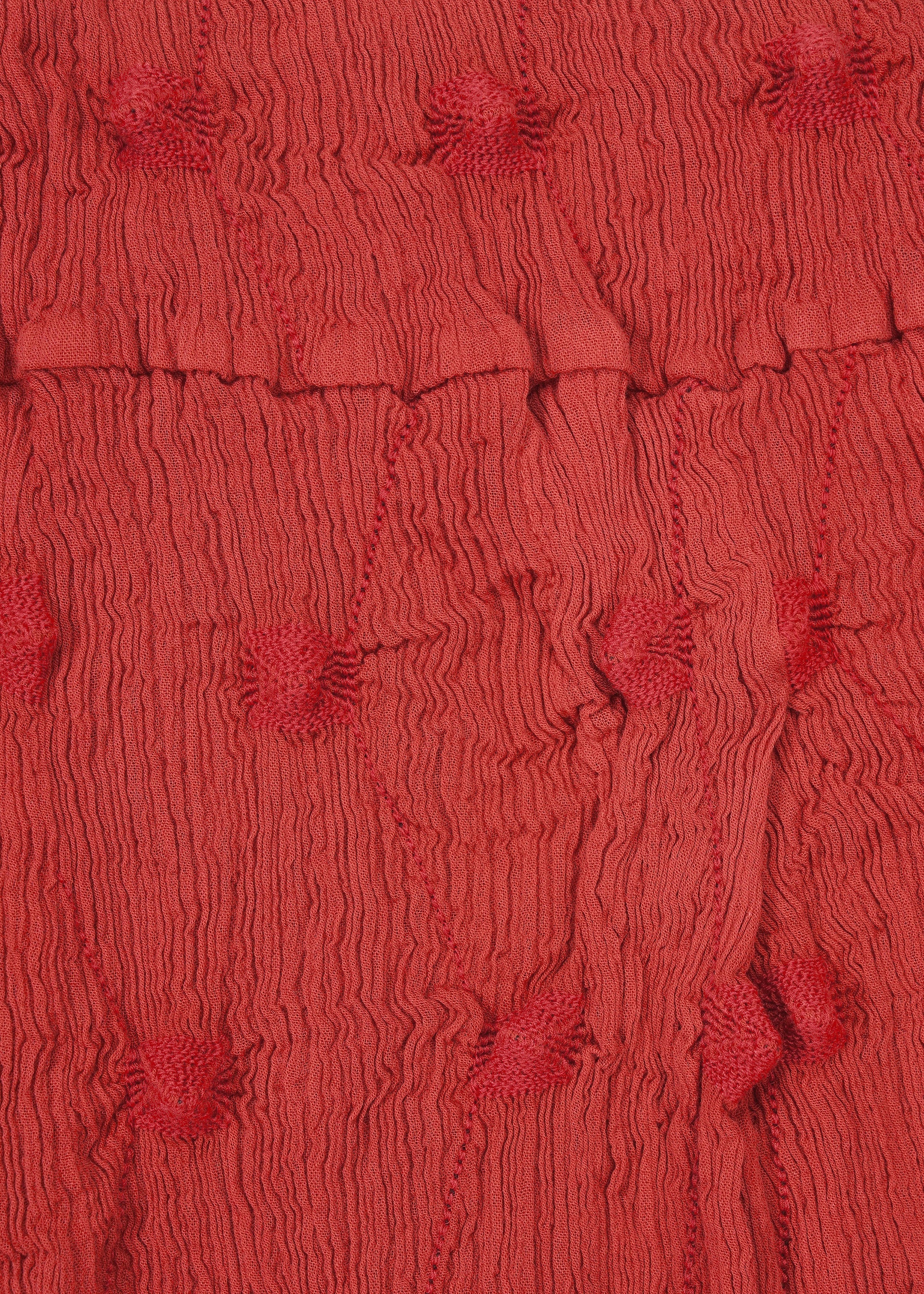 Zoomed view Crafted by HaaT, the KYO CHIJIMI SQUARE EMB features red textured fabric with a crinkled appearance and raised, round tufted dots evenly distributed across the surface. Reminiscent of classic KYO CHIJIMI pants, this material has a subtly uneven, gathered finish that enhances its distinctive crinkled texture, adding both depth and visual interest.