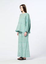 A woman in profile wears HaaT’s ONE STROKE DRAW: a loose, light teal patterned long-sleeve top with matching wide jacquard pants and black sandals, posed against a simple light backdrop.