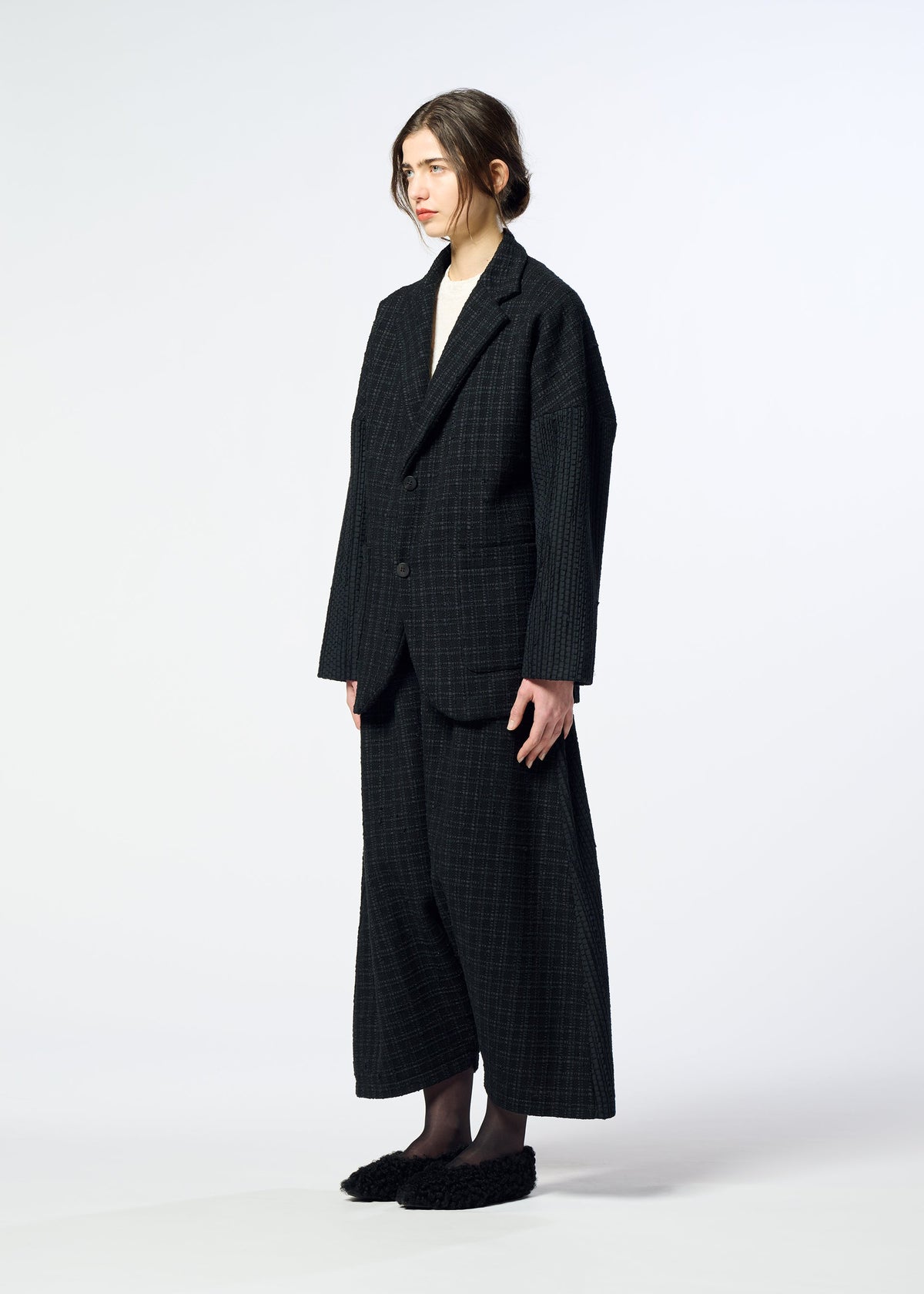 A person with light skin and brown hair in a loose bun wears the HaaT SAKIORI oversized dark plaid woven blazer and matching wide-leg pants, paired with black slippers against a plain background. view 9 of 10