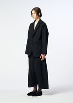 A person with light skin and brown hair in a loose bun wears the HaaT SAKIORI oversized dark plaid woven blazer and matching wide-leg pants, paired with black slippers against a plain background.