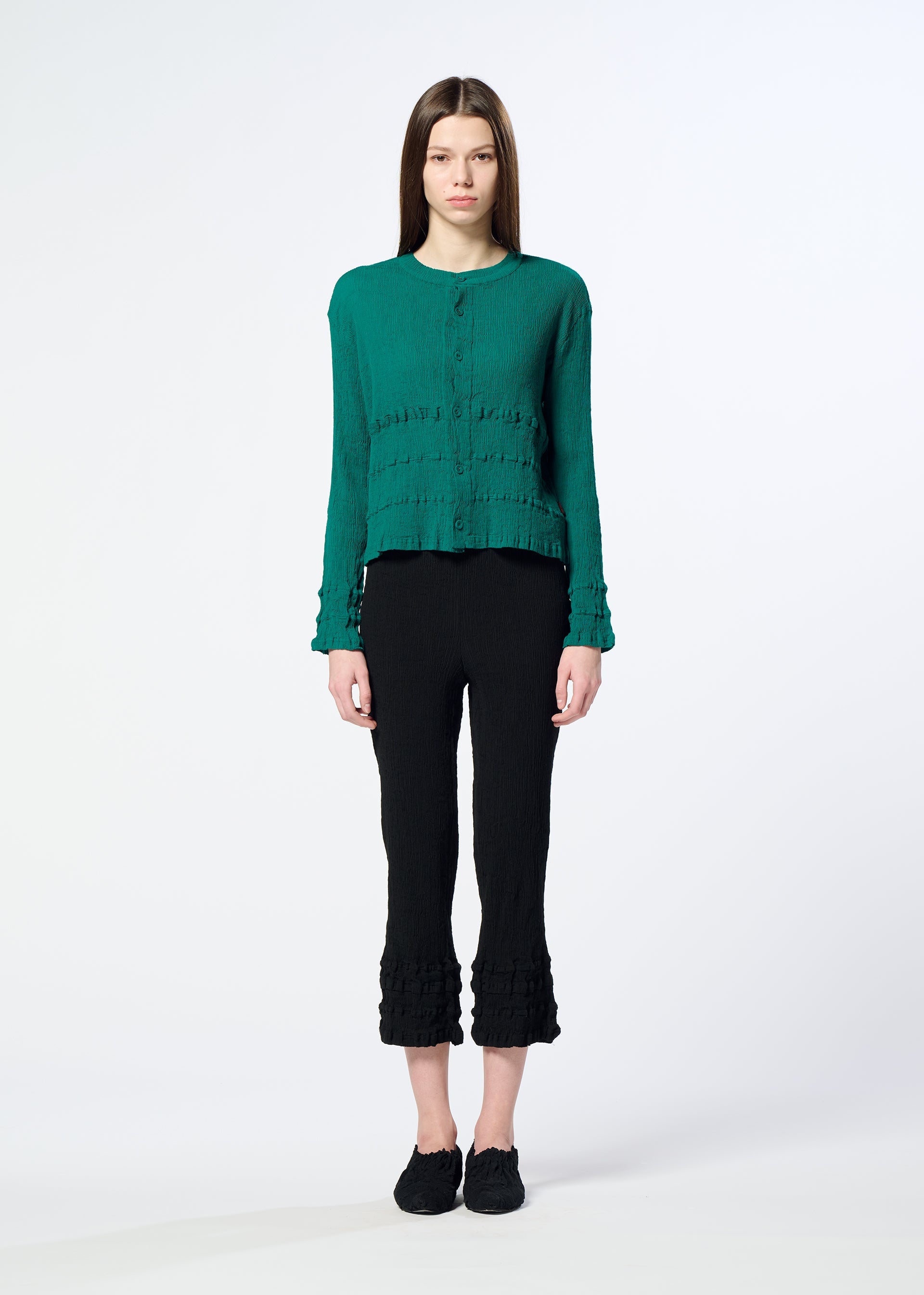 Zoomed view A person stands facing forward against a white background, wearing a green long-sleeve buttoned top, HaaT’s KYO CHIJIMI TSUCHIKABE pants with textured hems for a crepe-like feel, and black shoes.
