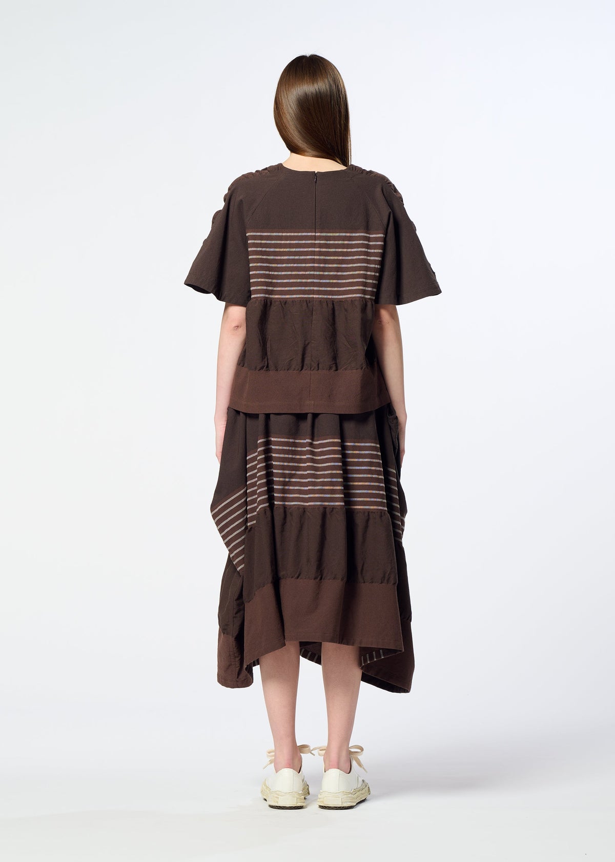 A person with long brown hair, dressed in HaaT’s COLLAGE STRETCH Ⅱ—a loose brown top paired with a voluminous skirt featuring horizontal colorful stripes—stands facing away from the camera against a plain white background. view 8 of 8