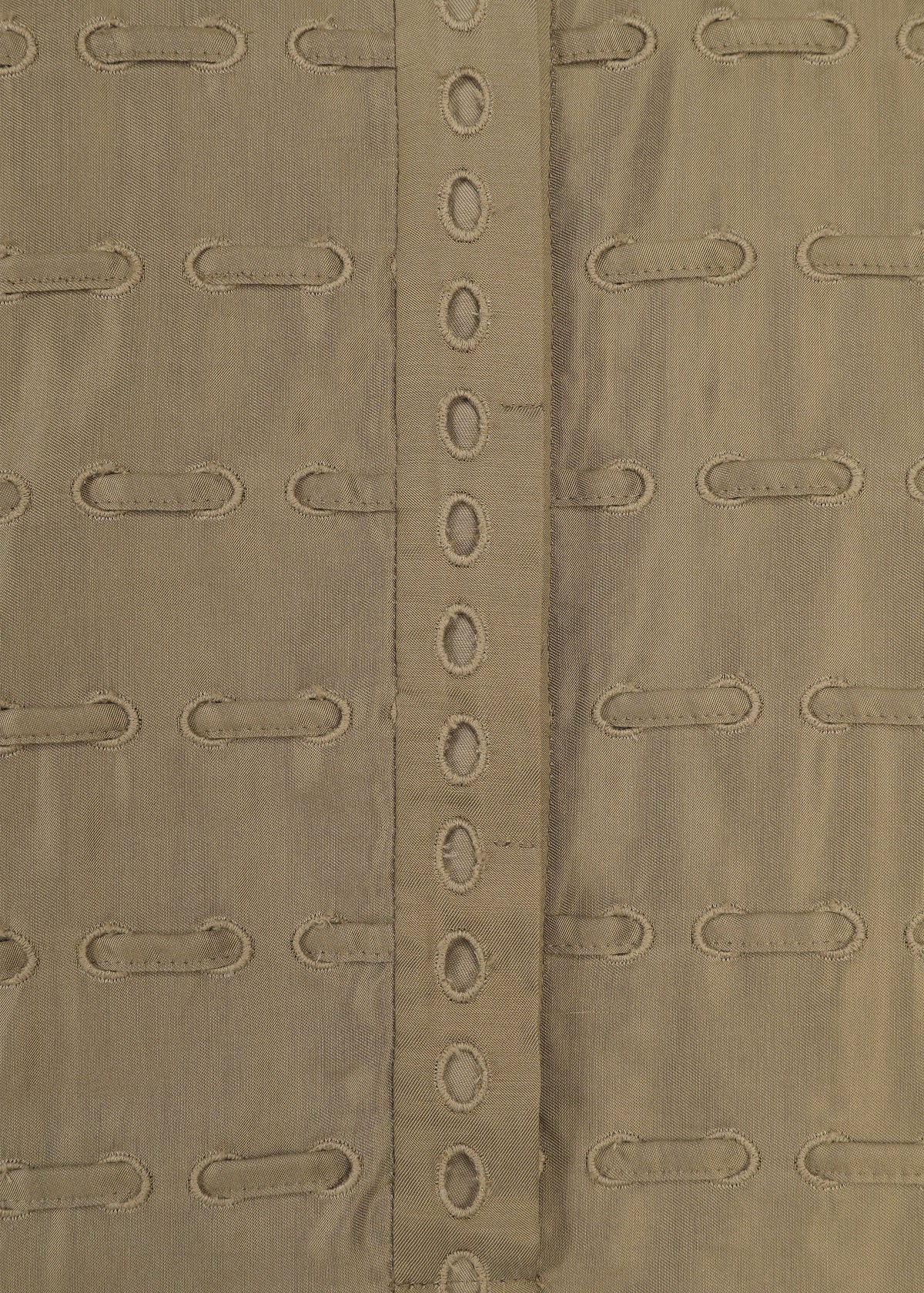 Close-up of the HOLE & LINE fabric by HaaT, showcasing tan or khaki twill material with horizontal embroidered oval cutouts and a vertical central strip adorned with a row of matching oval holes. This eyelet embroidery brings delicate detail to the soft texture and repeating pattern, evoking styles seen in poncho-style dresses. view 5 of 8
