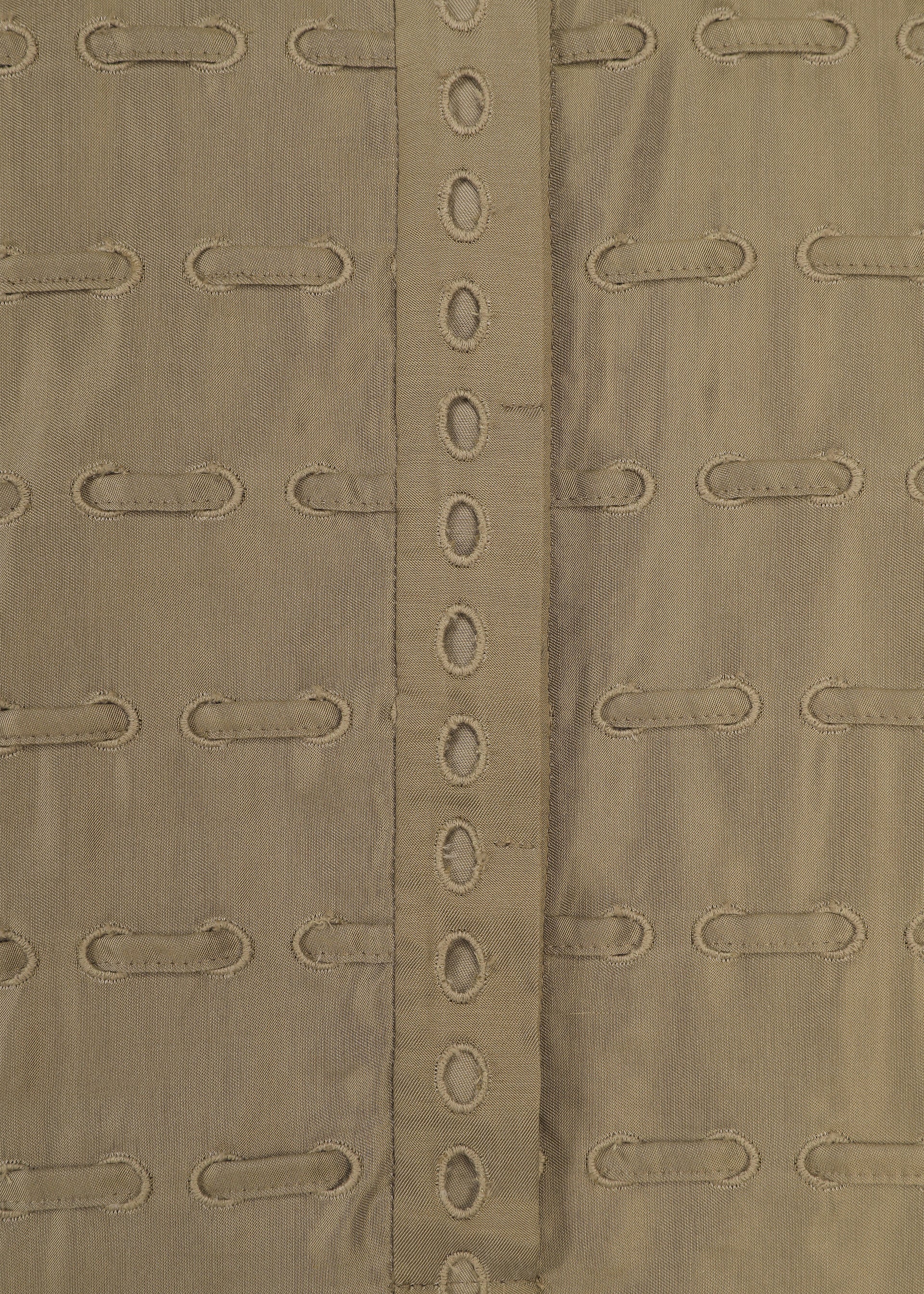 Zoomed view Close-up of the HOLE & LINE fabric by HaaT, showcasing tan or khaki twill material with horizontal embroidered oval cutouts and a vertical central strip adorned with a row of matching oval holes. This eyelet embroidery brings delicate detail to the soft texture and repeating pattern, evoking styles seen in poncho-style dresses.