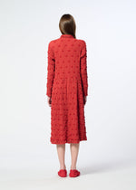 A woman with long brown hair wears the HaaT KYO CHIJIMI SQUARE EMB dress—a textured, red, long-sleeved midi style with a crinkled finish—paired with matching red shoes, standing facing away against a plain white background.