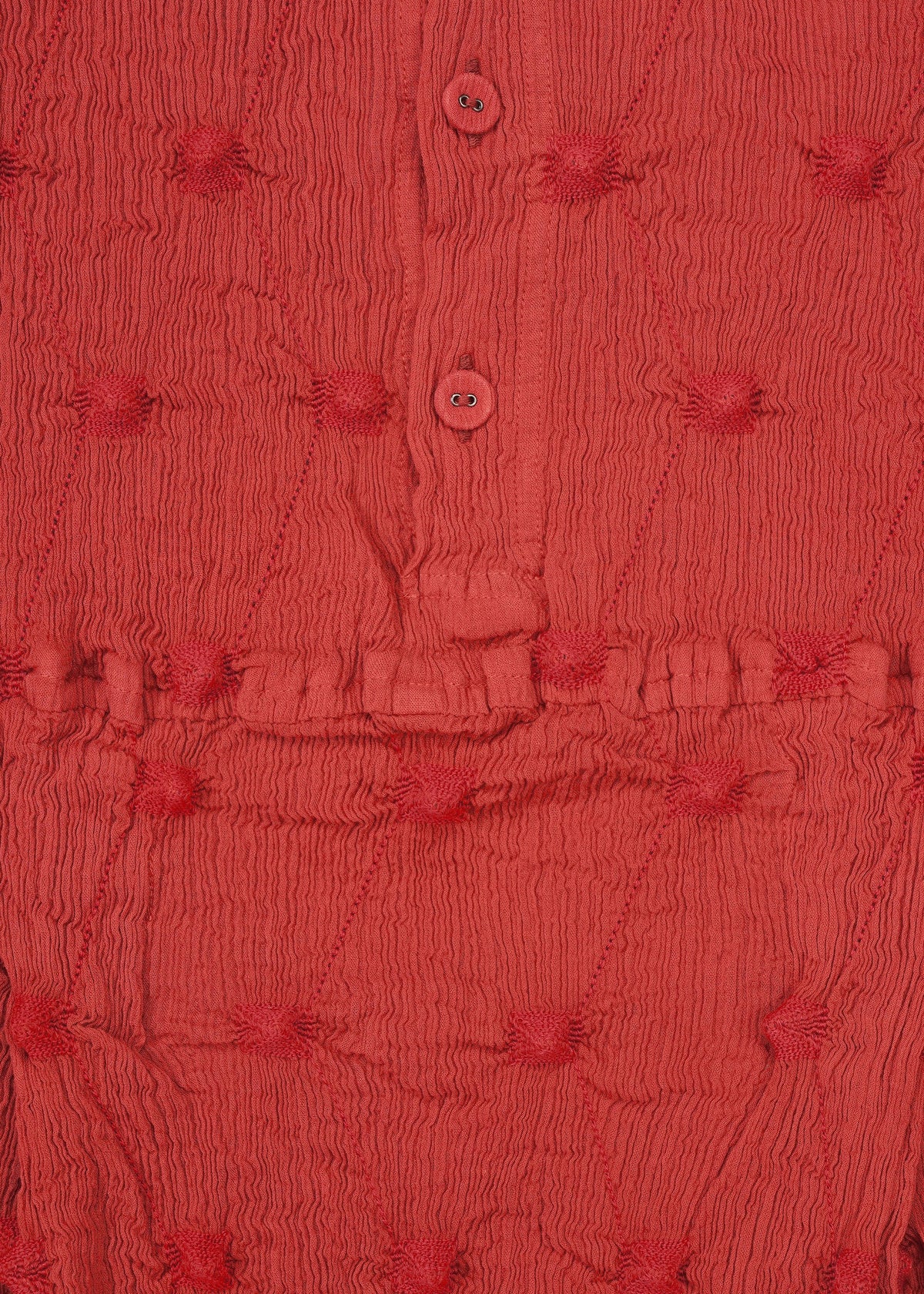 Close-up of textured red fabric featuring small, raised circular patterns, a horizontal stitched seam, and two red buttons on a button placket—evocative of the KYO CHIJIMI SQUARE EMB by HaaT with its signature crinkled texture. view 5 of 8