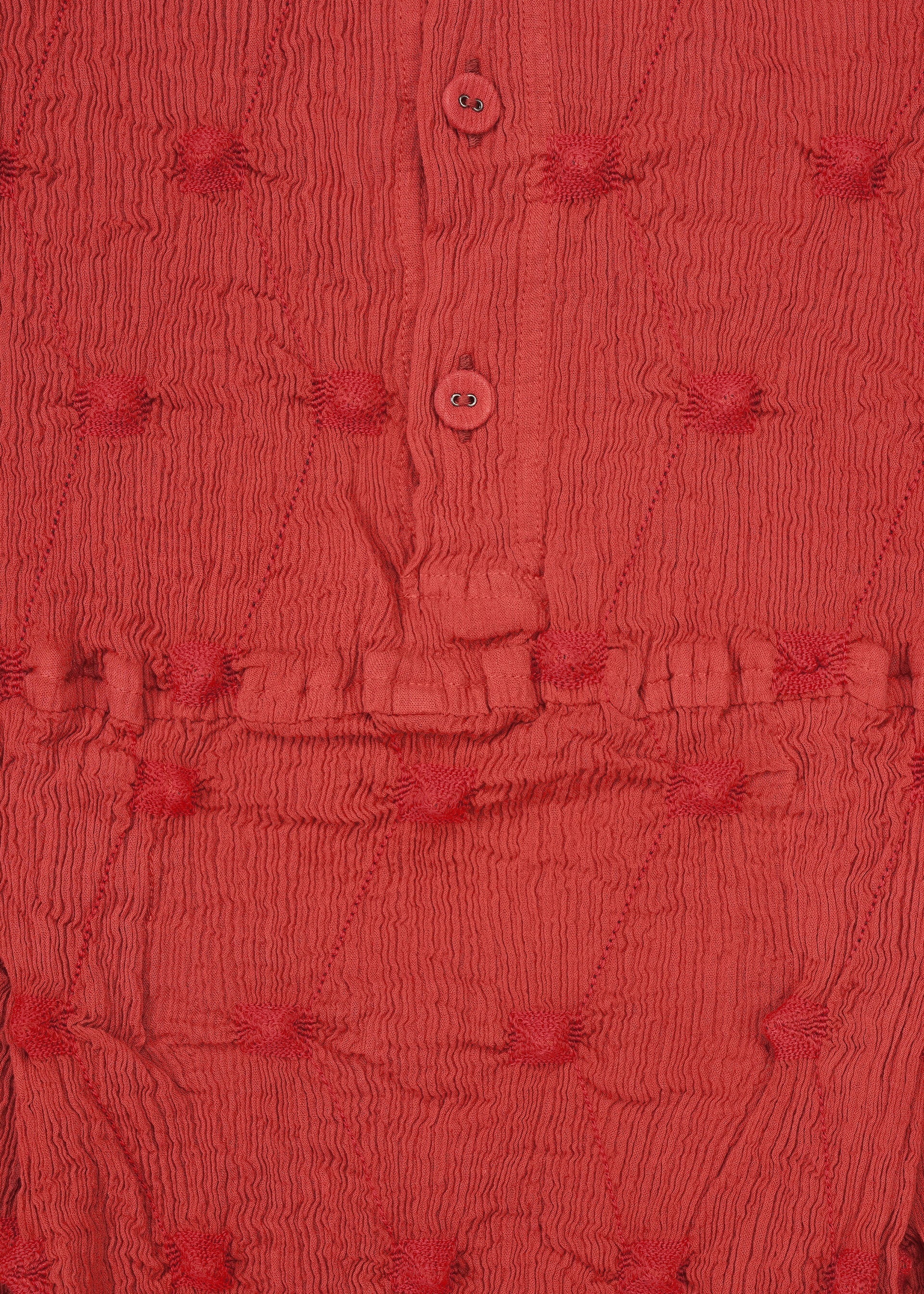 Zoomed view Close-up of textured red fabric featuring small, raised circular patterns, a horizontal stitched seam, and two red buttons on a button placket—evocative of the KYO CHIJIMI SQUARE EMB by HaaT with its signature crinkled texture.