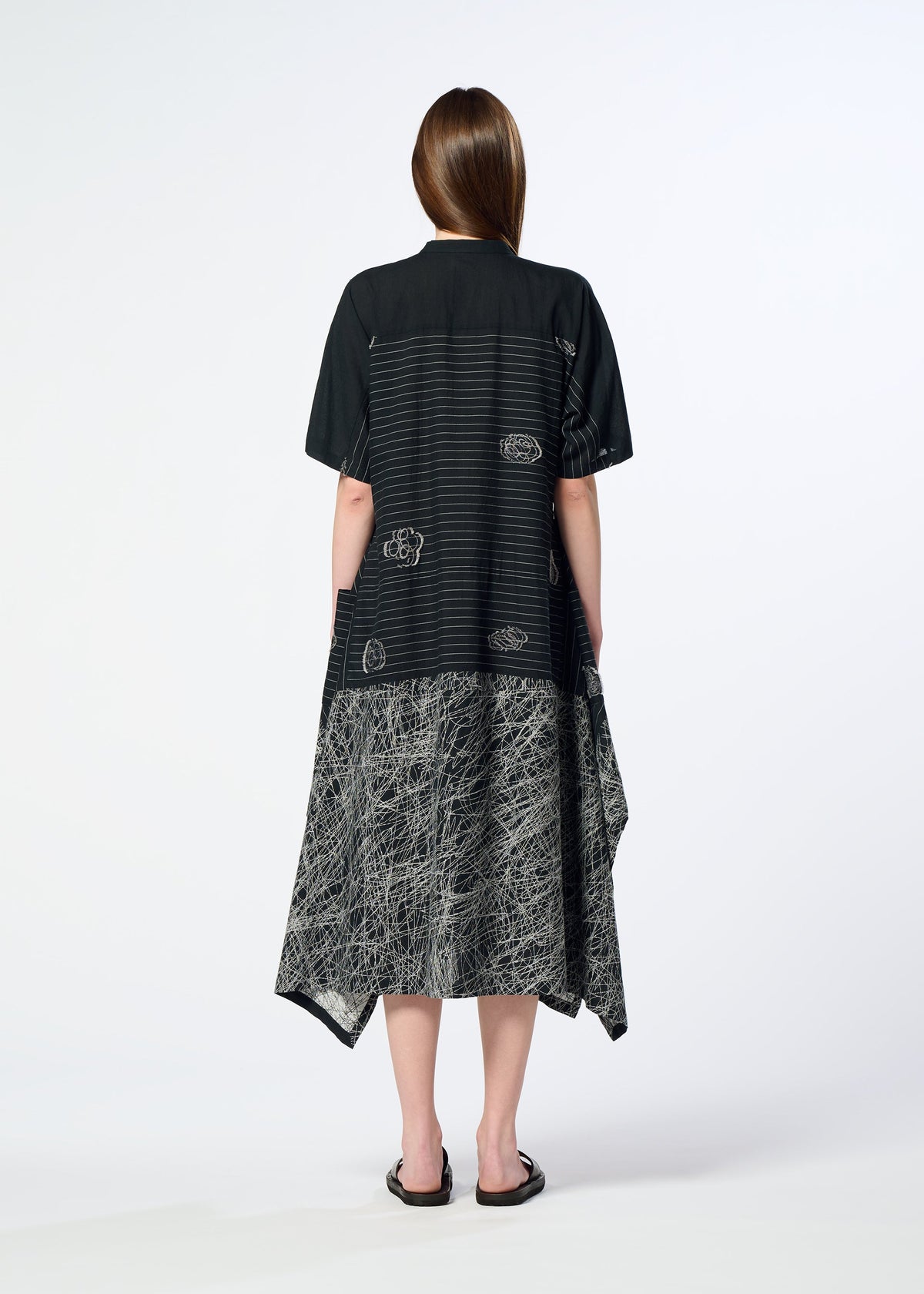A woman with straight brown hair faces away, wearing the HaaT ONE STROKE DRAW jacquard dress with abstract white patterns, loose short sleeves, and a mid-calf length, styled simply with black sandals. view 9 of 9