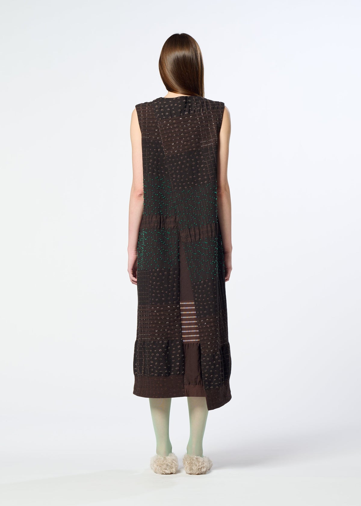 A person with long brown hair, seen from behind against a plain white background, is wearing the HaaT COLLAGE STRETCH Ⅰ— a sleeveless dark brown midi dress with jacquard-textured patterns—paired with light green tights and fluffy slippers. view 8 of 8