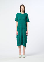 A woman with straight brown hair wears the HaaT KYO CHIJIMI TSUCHIKABE dress featuring textured horizontal bands and ruffled details, standing against a plain light background.