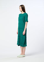 A woman stands sideways in a simple green KYO CHIJIMI TSUCHIKABE dress by HaaT with short sleeves and light green slip-on shoes, set against a plain white background.