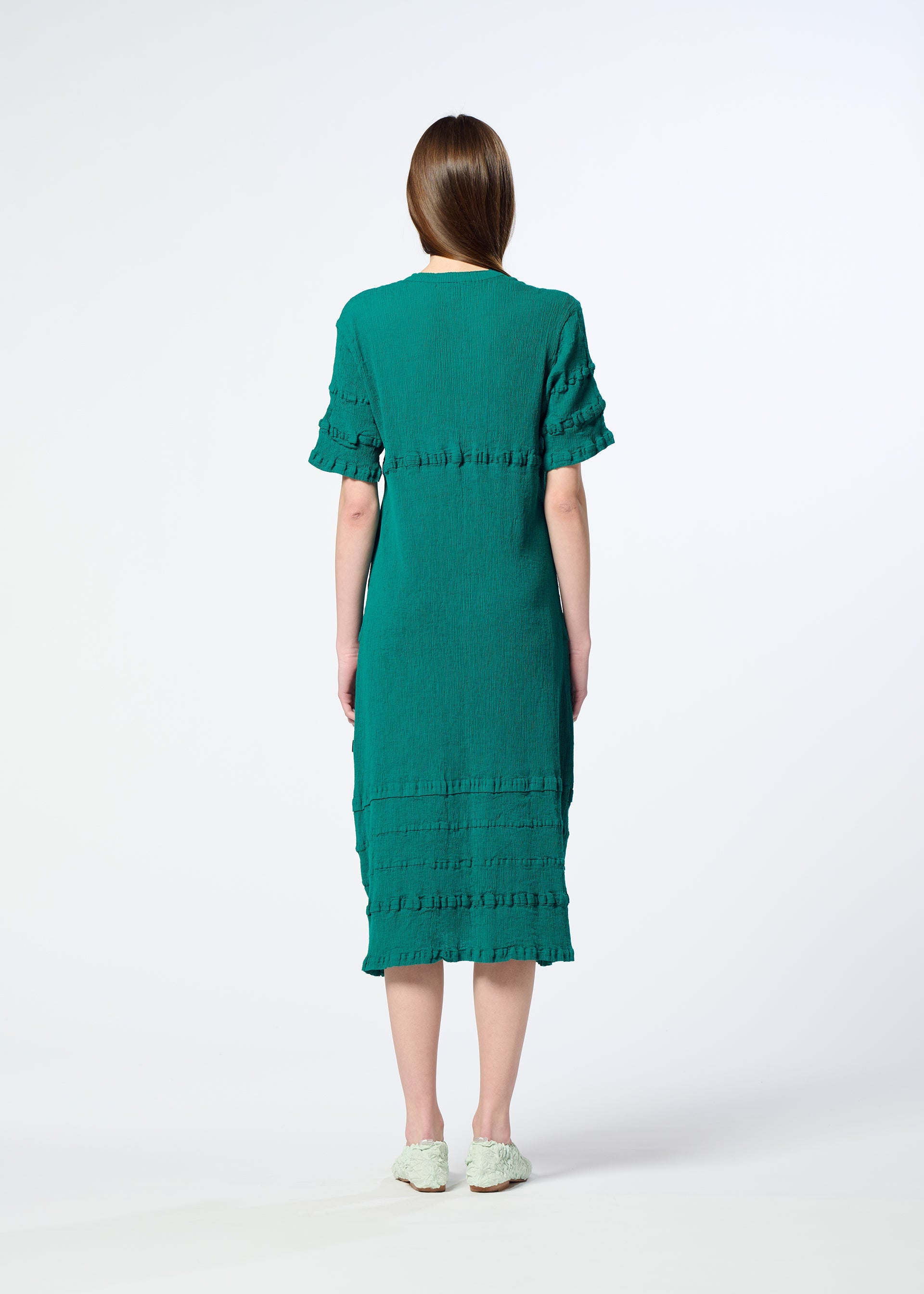 Zoomed view A woman with straight brown hair, seen from behind, wears a teal KYO CHIJIMI TSUCHIKABE dress by HaaT with textured horizontal details and light-colored flats, standing against a plain white background.