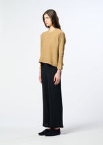 A person with long brown hair stands sideways against a plain white background, wearing HaaT’s KYO CHIJIMI 2WAY loose tan round-neck long-sleeved top and wide black pants paired with black shoes.