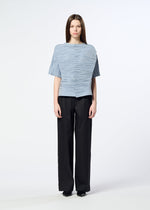 A person with long brown hair stands facing forward against a plain white background, wearing the HaaT SHIBARI SHIRT—a light blue textured short-sleeved top crafted from recycled polyester—paired with black wide-leg pants and black shoes.