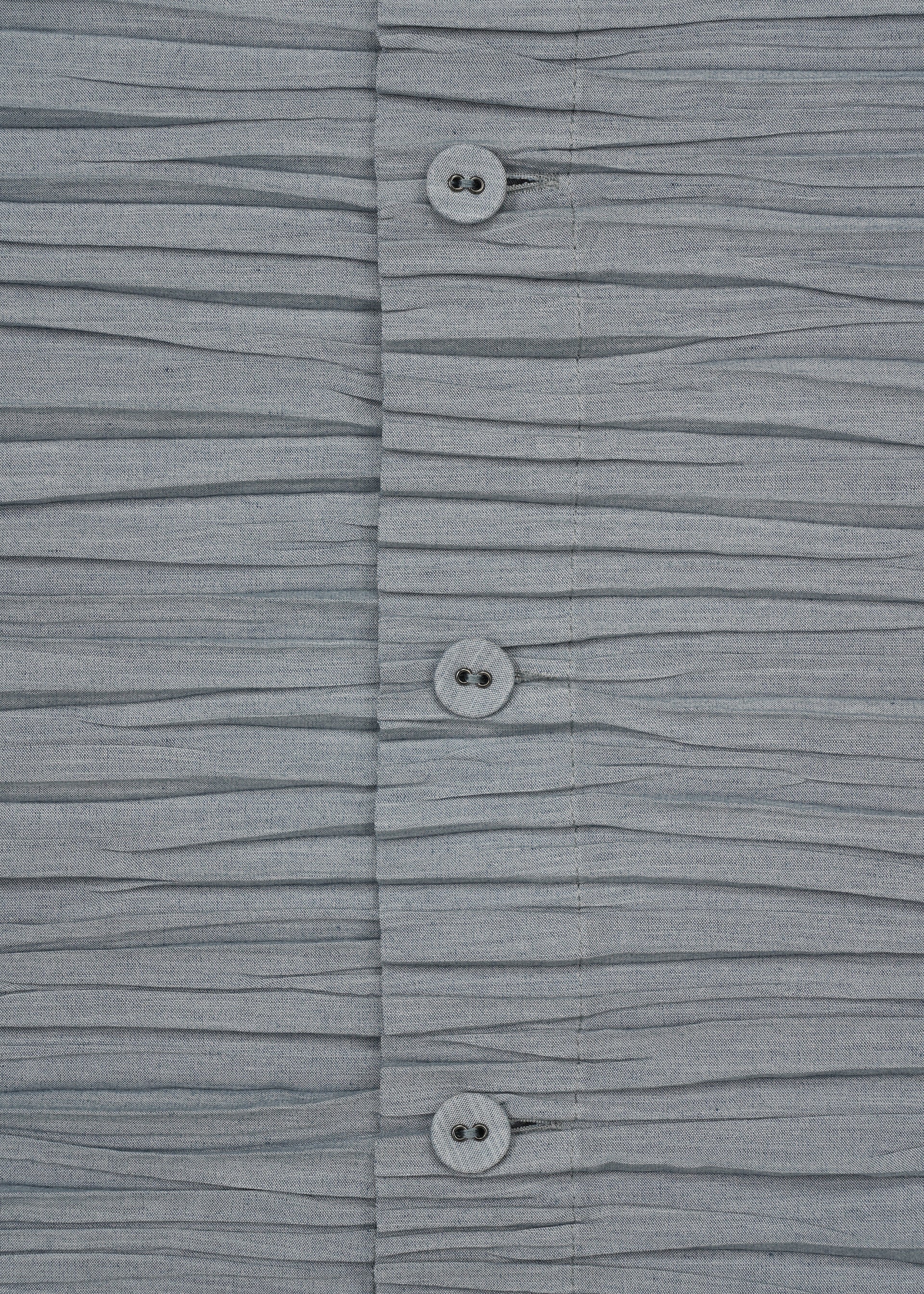 Zoomed view Close-up of the SHIBARI SHIRT by HaaT, a gray short-sleeved top featuring horizontal pleats and three buttons in the center. Crafted from recycled polyester for an eco-friendly touch, its soft texture and pleated arrangement create a wavy effect across the material.