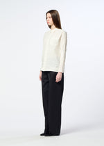 A person stands against a plain background wearing the HaaT SHIBARI SHIRT—a textured white long-sleeved shirt with a subtle Shibari finish—paired with wide black pants and black shoes.