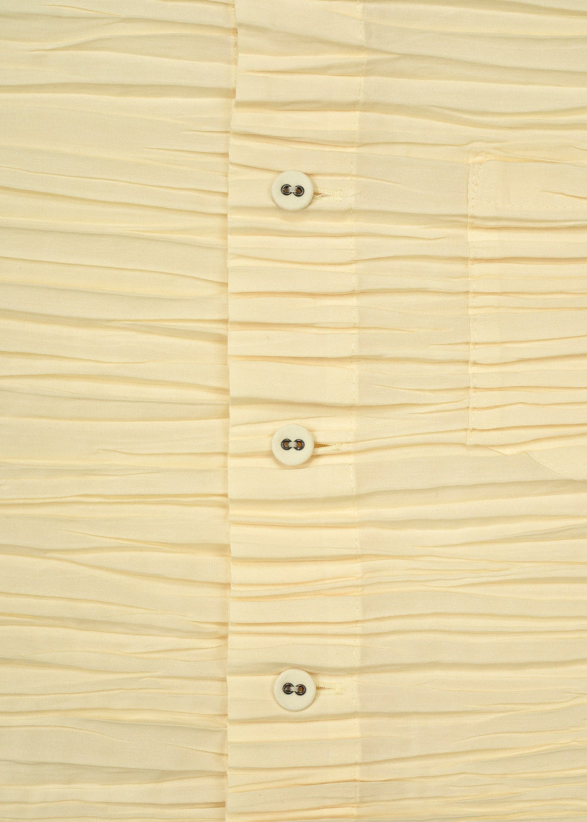 Close-up of the SHIBARI SHIRT by HaaT, a cream-colored, pleated long-sleeved shirt crafted from recycled polyester, featuring four white buttons, visible stitching, and part of a pocket on the right side. view 6 of 9