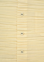 Close-up of the SHIBARI SHIRT by HaaT, a cream-colored, pleated long-sleeved shirt crafted from recycled polyester, featuring four white buttons, visible stitching, and part of a pocket on the right side.