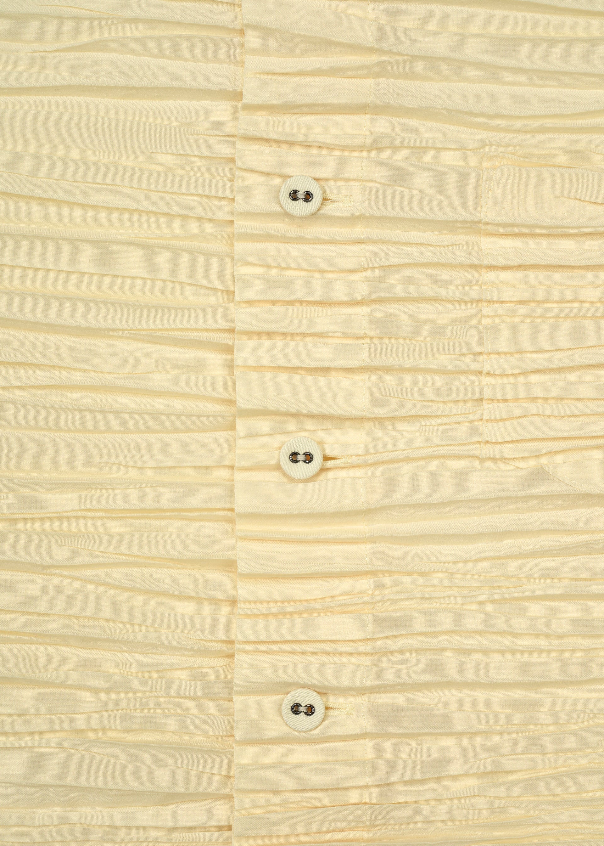 Zoomed view Close-up of the SHIBARI SHIRT by HaaT, a cream-colored, pleated long-sleeved shirt crafted from recycled polyester, featuring four white buttons, visible stitching, and part of a pocket on the right side.