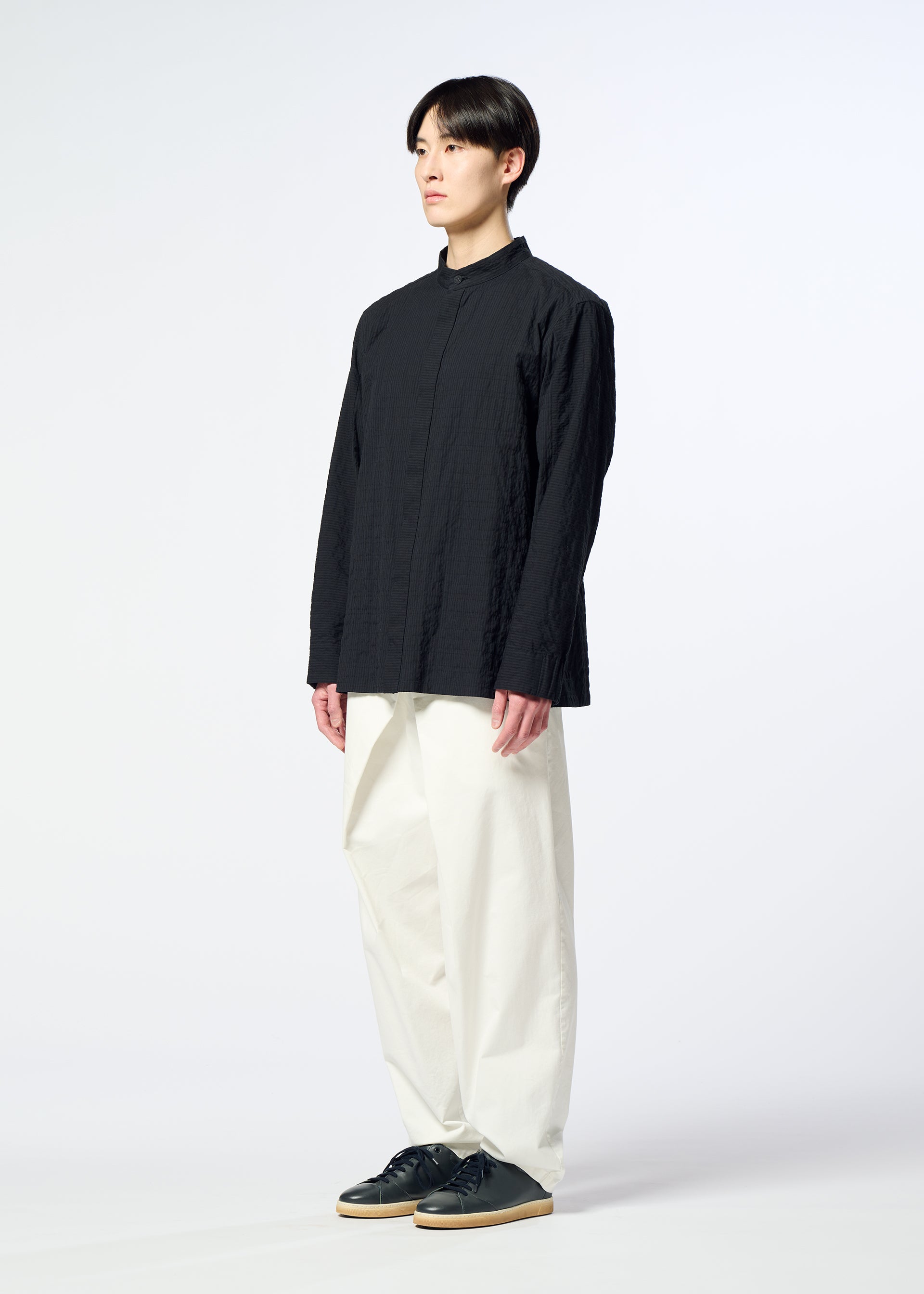 Zoomed view A person stands against a plain white background, wearing HaaT’s RIPPLE STRIPE black long-sleeved shirt, loose white pants, and black shoes, looking forward with a neutral expression.