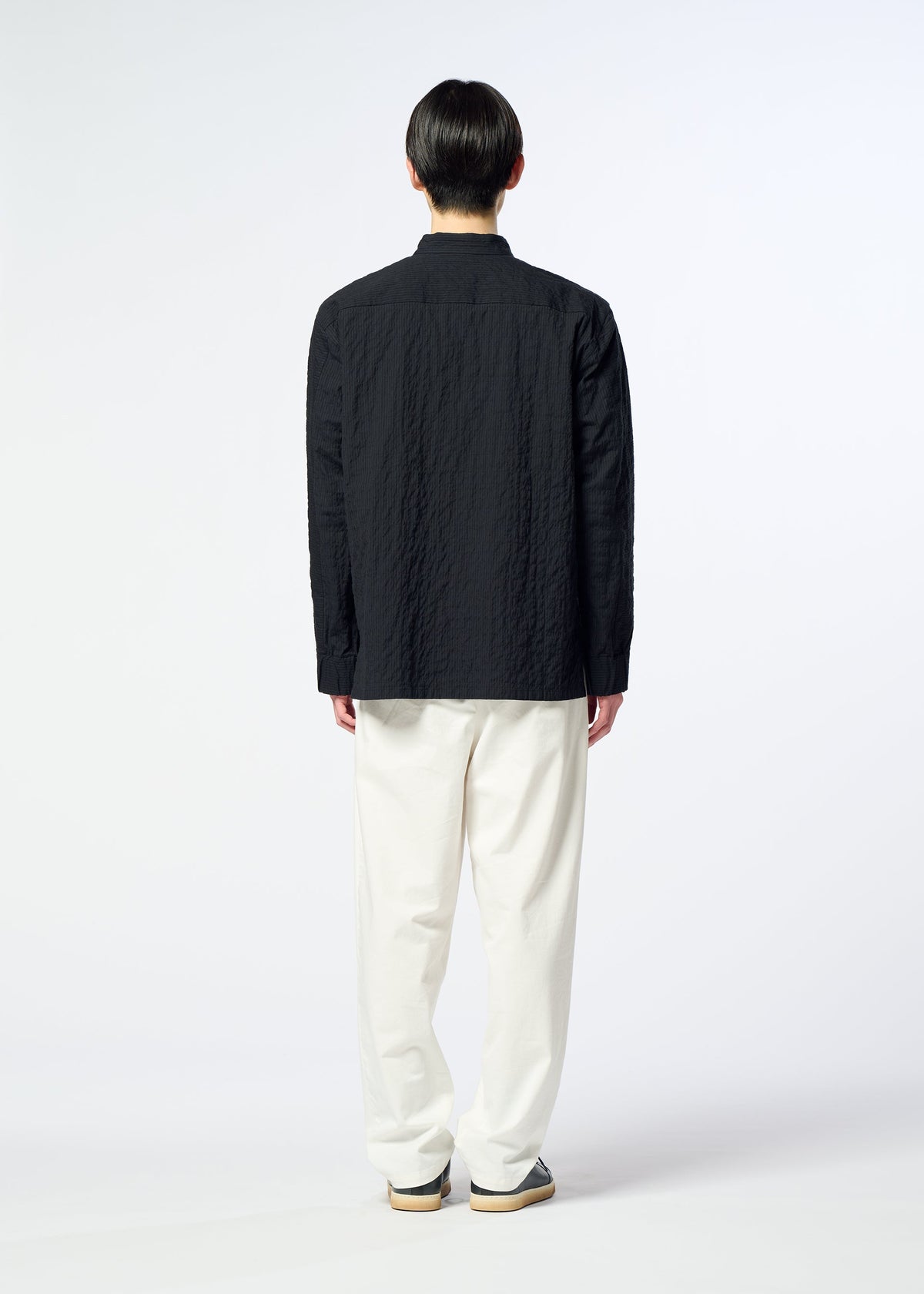 A person stands facing away, wearing HaaT’s RIPPLE STRIPE textured black seersucker shirt with long sleeves, paired with white loose pants and sneakers, set against a plain light background. view 11 of 11