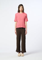 A person stands against a plain white background wearing the HaaT KYO CHIJIMI AUGUST short-sleeve top, crafted from ultra-fine cotton with a subtle crinkled texture, paired with wide-leg brown pants and beige shoes.