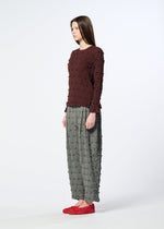A woman stands sideways against a plain light background, wearing the HaaT KYO CHIJIMI SQUARE EMB textured maroon top paired with gray wide-legged textured pants and red shoes.