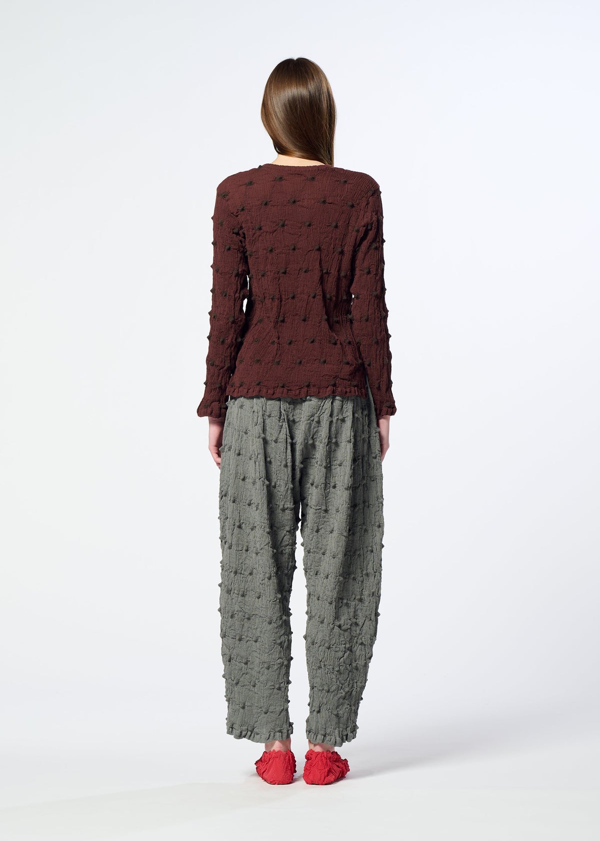 Wearing the KYO CHIJIMI SQUARE EMB top by HaaT, a person stands with their back to the camera in a crinkled brown shirt, loose gray textured pants, and red shoes against a plain white background. view 8 of 8