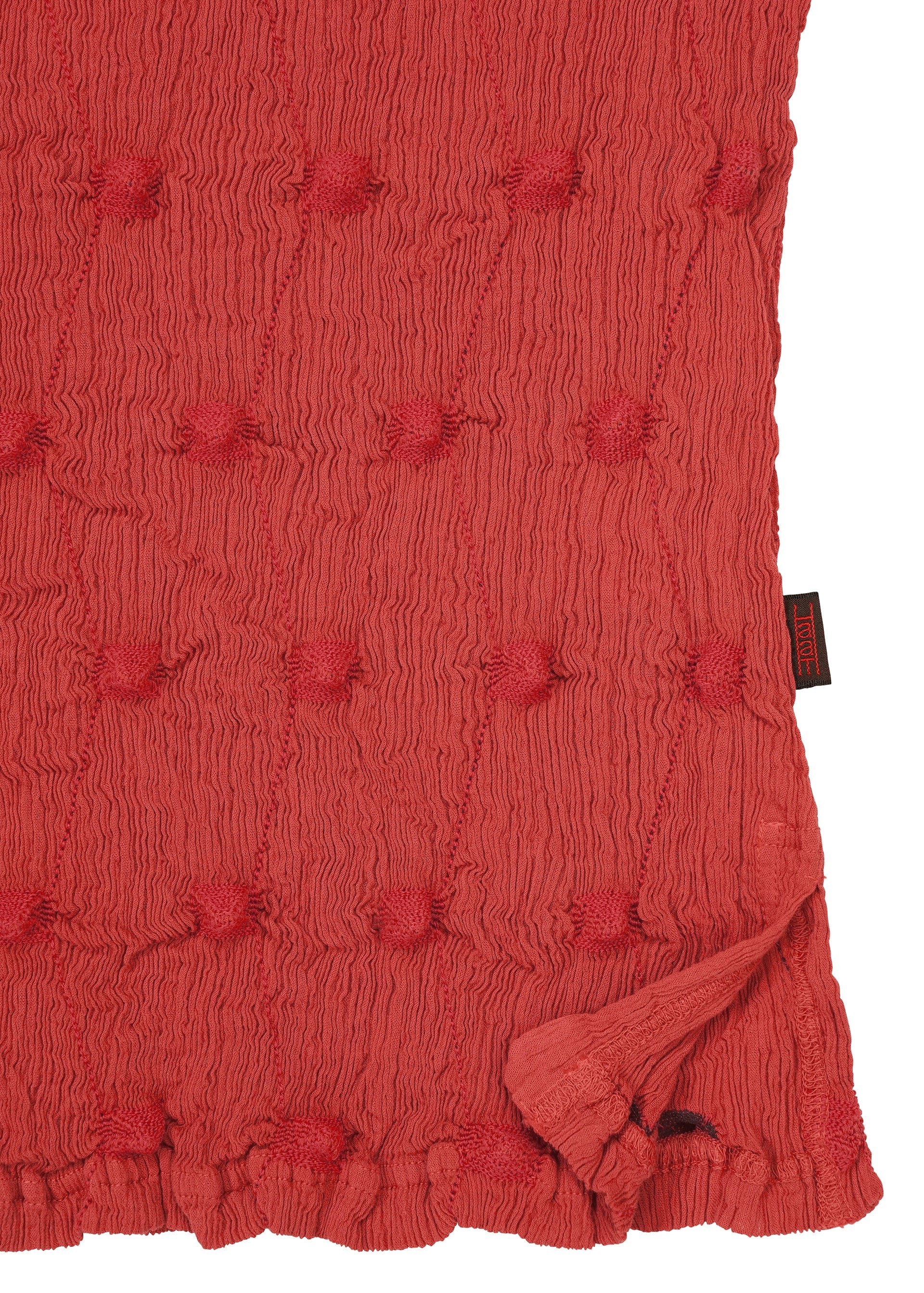 Zoomed view A textured red KYO CHIJIMI SQUARE EMB top by HaaT featuring a crinkled finish with raised, tufted dots and a subtly ruffled edge. A black and red HaaT tag is sewn into the right seam.