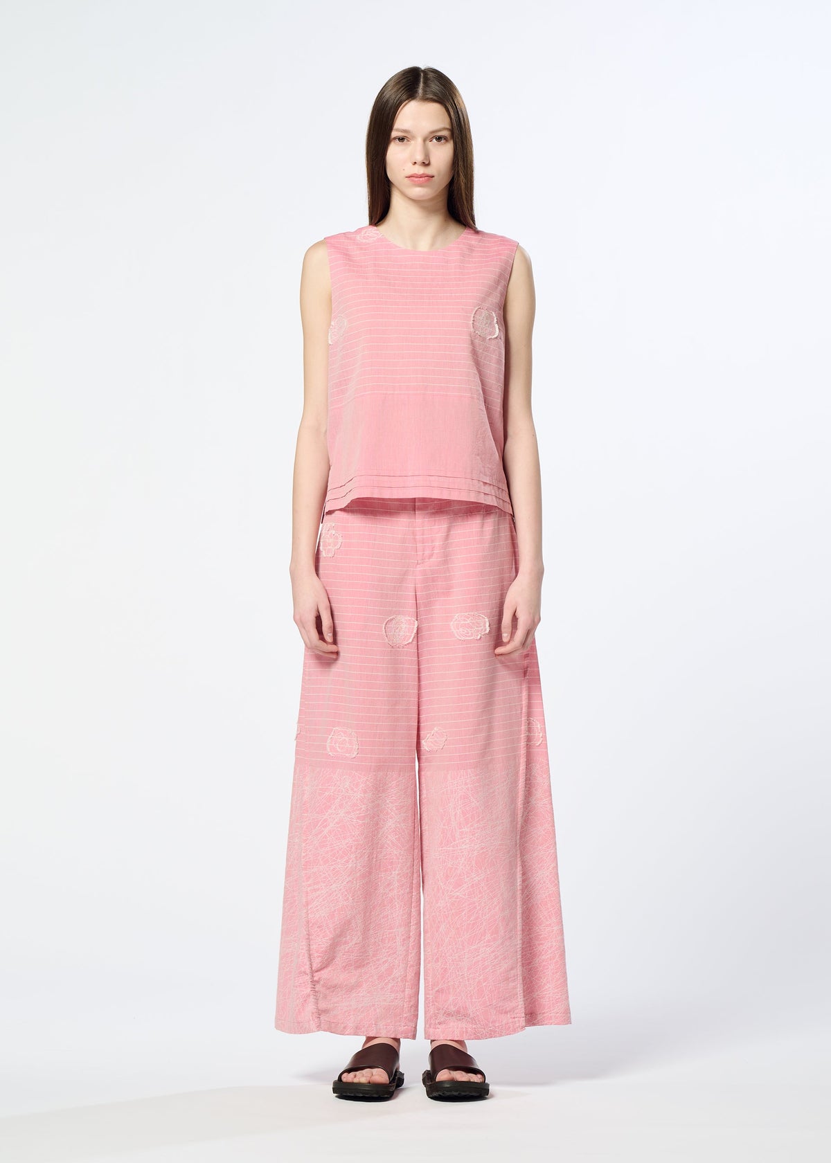 A woman with straight brown hair wears HaaT's ONE STROKE DRAW jacquard sleeveless top and matching wide-leg pants in a cotton-cupra blend, featuring subtle three-dimensional patterns. She pairs them with black sandals against a white background. view 4 of 6