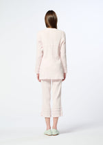 A woman faces away, wearing HaaT’s KYO CHIJIMI TSUCHIKABE light pink pajama set with a crepe-like texture and ruffle details, paired with mint green slippers, against a plain white background.