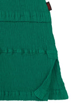 Close-up of the green KYO CHIJIMI TSUCHIKABE top by HaaT, featuring a crepe-like textured fabric with horizontal pleats, side slit, and a small black and red label at the top edge. Made from ultra-fine cotton.