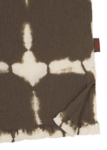 A close-up of the KYO CHIJIMI PACKAGE DYE cotton top by HaaT shows brown and white tie-dye patterns crafted by Kyoto artisans, with a folded corner revealing the unique design and a small black and red tag.