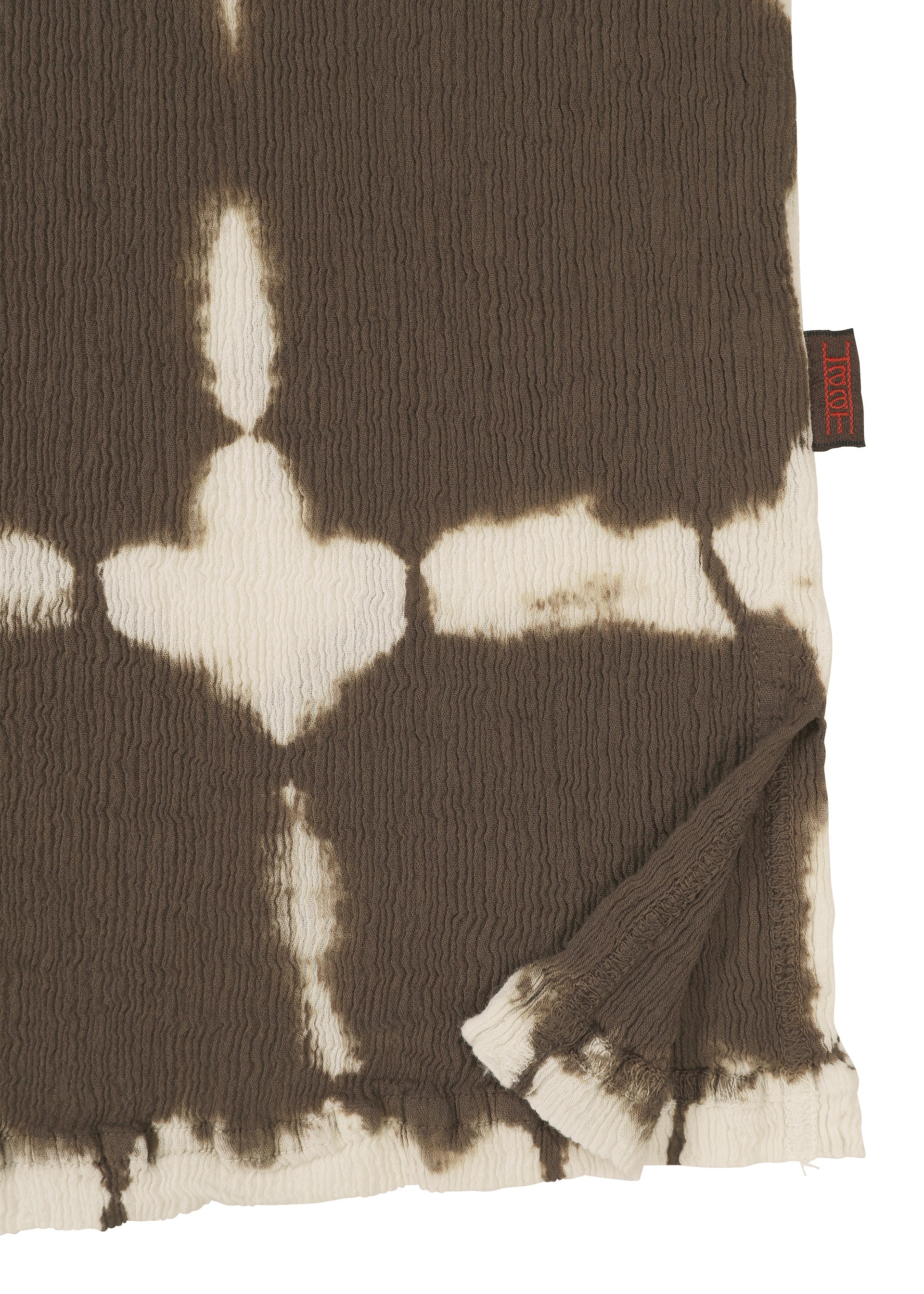 Zoomed view A close-up of the KYO CHIJIMI PACKAGE DYE cotton top by HaaT shows brown and white tie-dye patterns crafted by Kyoto artisans, with a folded corner revealing the unique design and a small black and red tag.